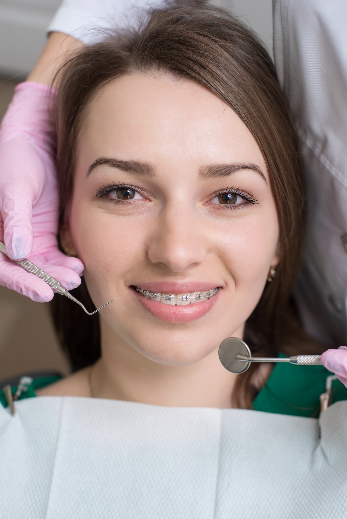 Portrait of happy female patient with metal braces. Orthodontist holding dental tools. Dentistry.